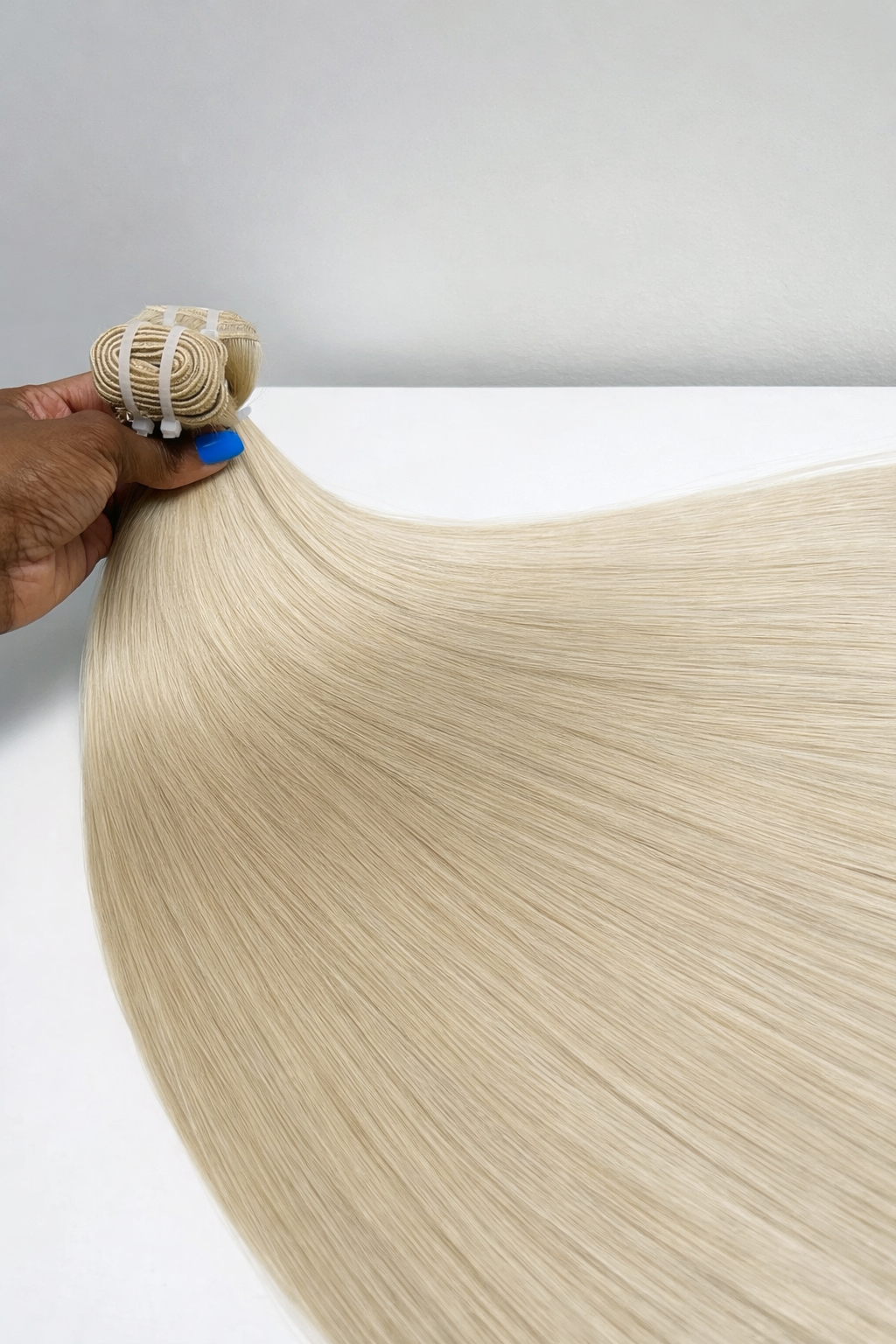 Blonde hair extensions being held above a white surface